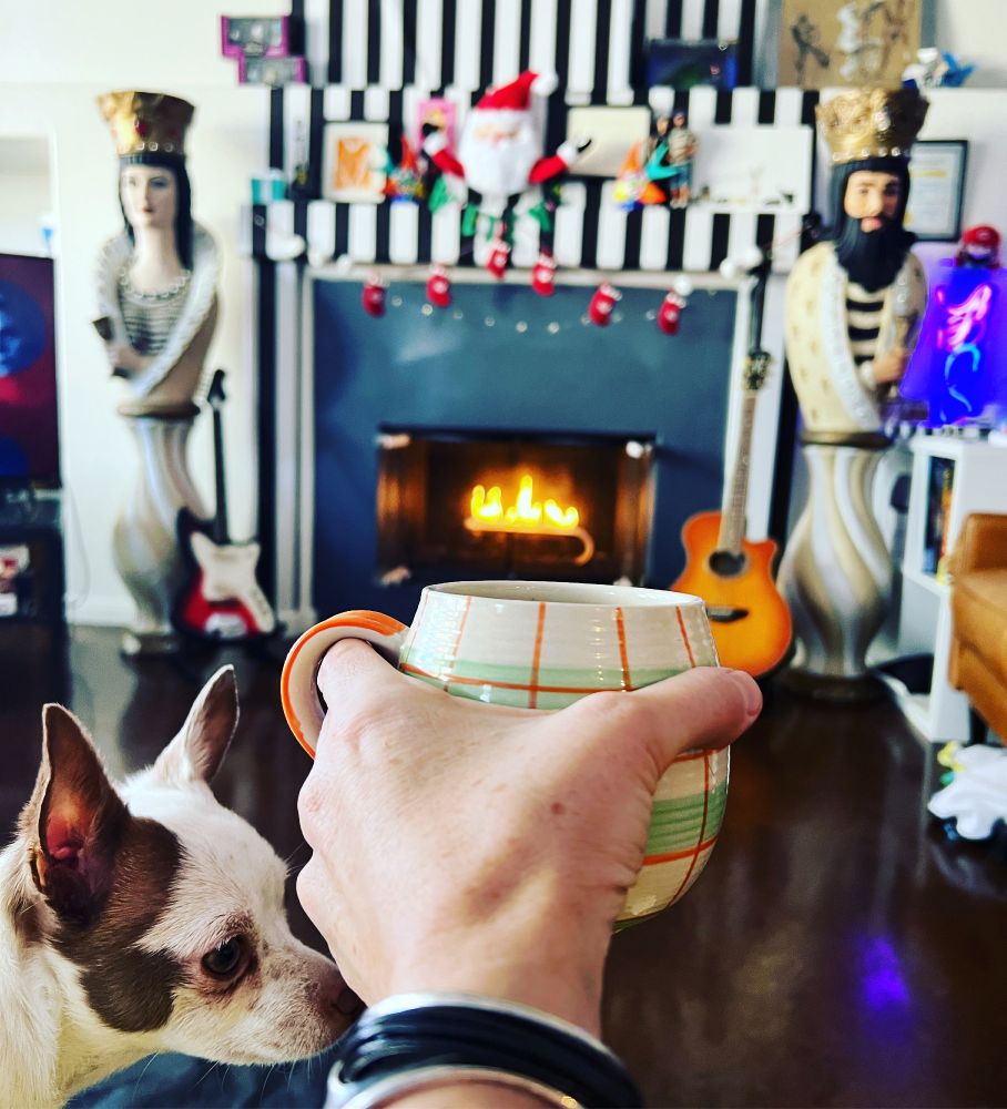 A hot cup of coffee in front of a warm fire in my living room, little Ernesto Esteban the rescue Chihuahua is peeking in from the side.
