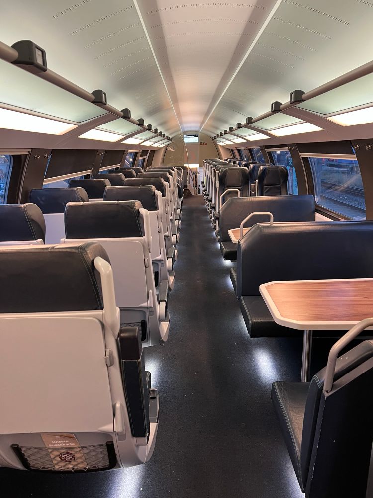 Innenraum des Zuges im Oberdeck mit 2+2-Bestuhlung mit Ledersitzen. Auf der rechten Seite flache Sitzbänke mit großen Tischen, links „normale“ Doppelsitze.