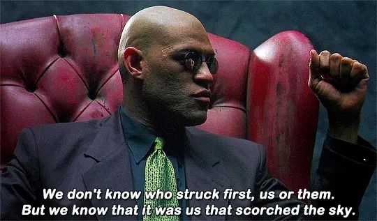 A dark skinned man in a black jacket, green tie, sitting in a red chair with the text " we don't know who struck first us or them, but we know that it was us that scorched the sky" in white text on the bottom.