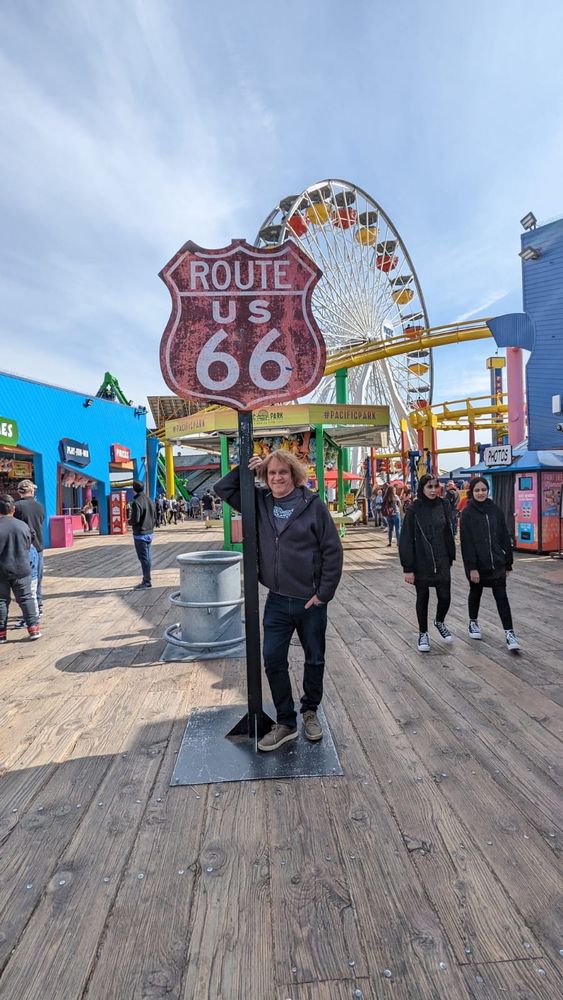 Singer-songwriter Johnny Schaefer on the pier in Santa Monica, CA in front of a sign that says "Route 66"