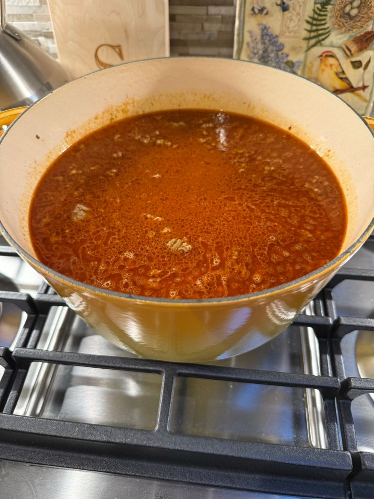A pot of chili simmering on a cooktop.

