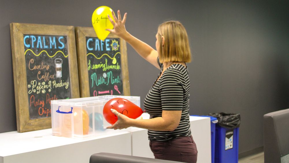A woman tapping a balloon in the air with a math problem written on the balloon.