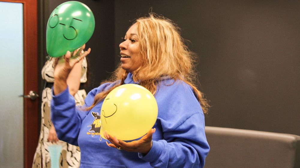 A woman with a balloon in each hand. The balloons have math problems written on them in marker. 