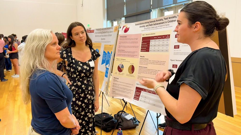 Caitlyn Lucy and Annie McIlroy discuss their research poster with an attendee at the undergraduate research symposium.