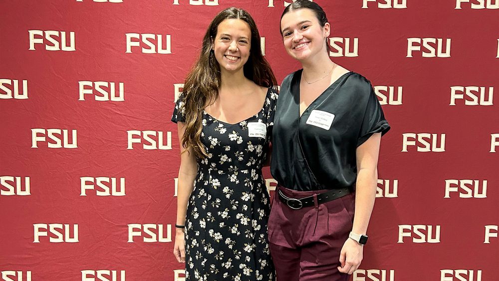 Caitlyn Lucy and Annie McIlroy pose in front of an FSU branded backdrop.