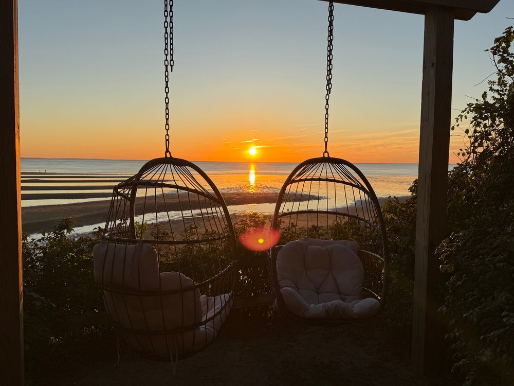 Two swinging chairs in front of a sunset on Cape Cod Bay. 