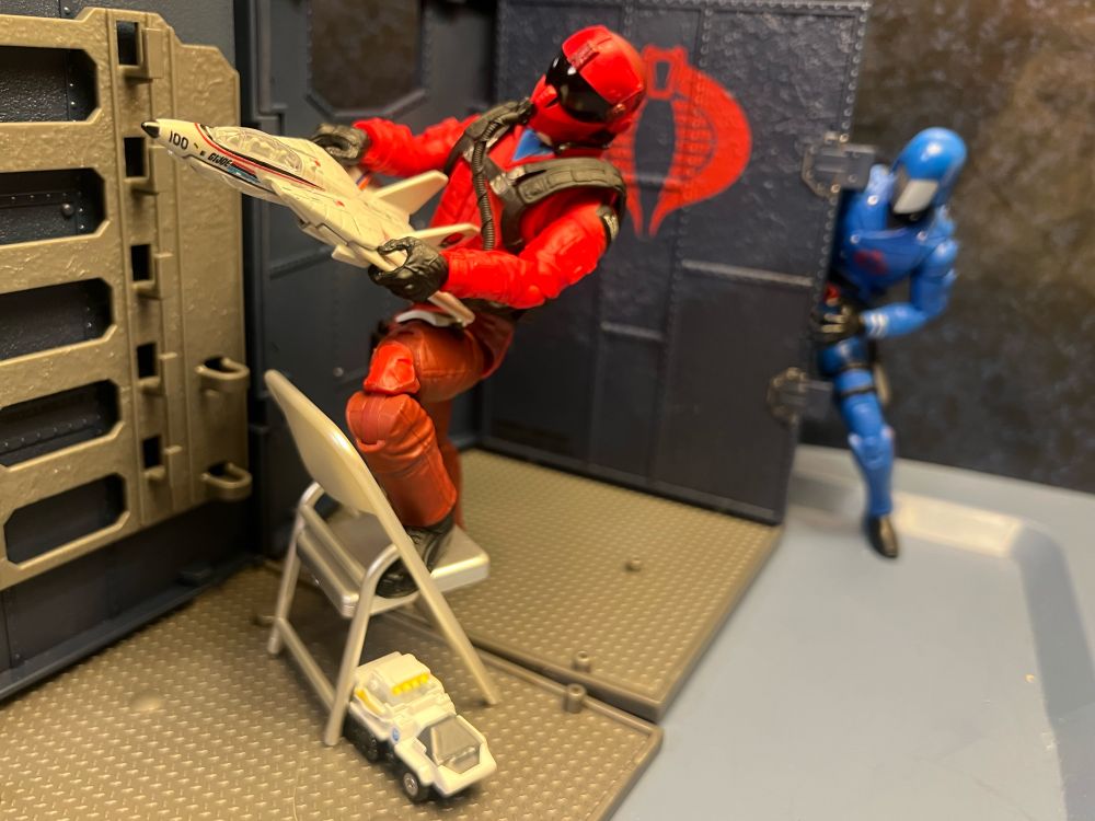 Wild Weasel enjoys cruising around a toy Skystriker, the jet piloted by his rival, ACE. There’s a toy Snowcat. Cobra Commander is peeking at this fun display.