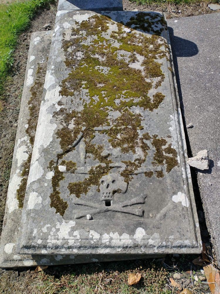 A lichen covered grave slab with prominent skull and crossbones.