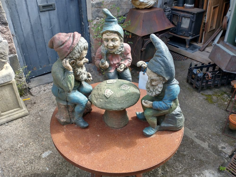 Sculpture of three garden gnomes playing cards on a mushroom table.