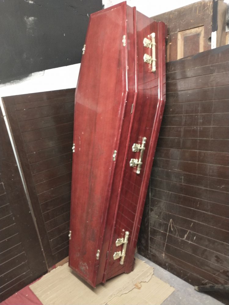Wooden coffin leaning upright against a brick wall.