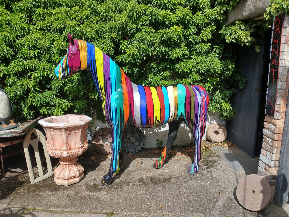 A statue of a horse covered in many stripes of paint of different colours.