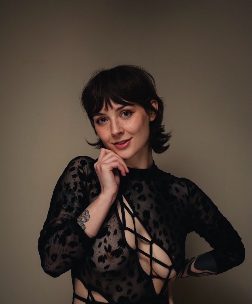 A portrait of Ayala wearing a black, cheetah print, mesh catsuit. Portions of the catsuit show lots of skin like fishnets all the way down their body. Their eyes twinkle brightly, their hair & freckles look so cute. You find yourself to be magnetized and mesmerized. You know what you must do. You can’t resist. You check out the links in their bio and subscribe to their Onlyfans 