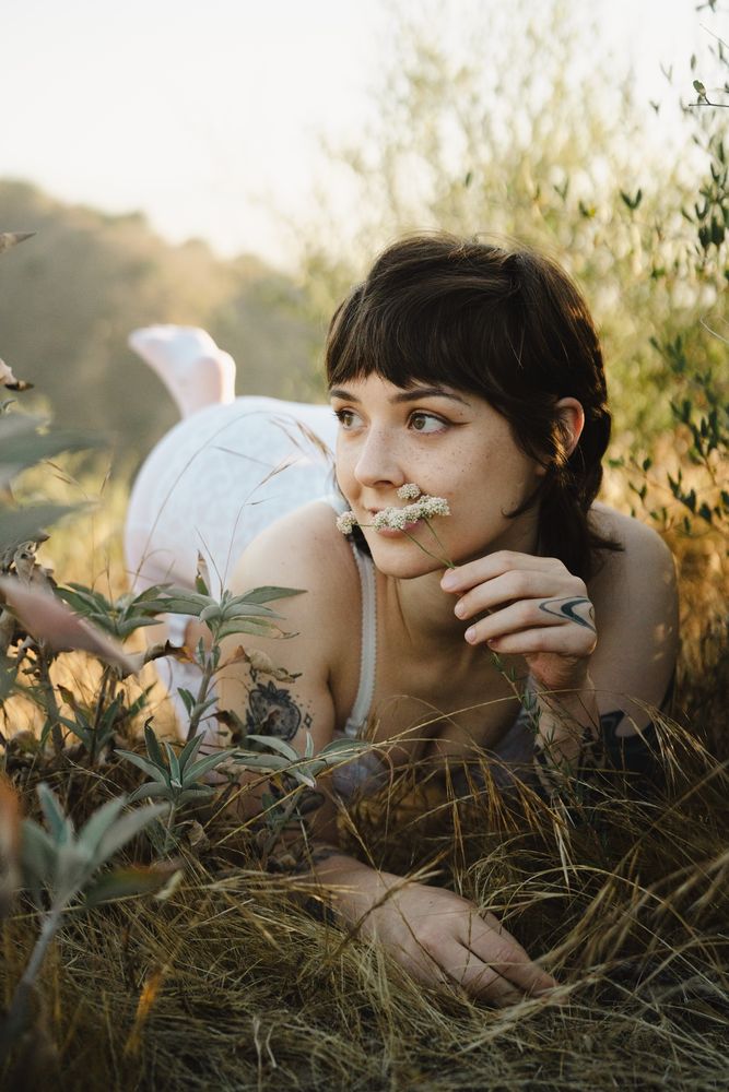 Ayala is seen in white delicate lingerie laying in the tall grass, smelling little white flowers