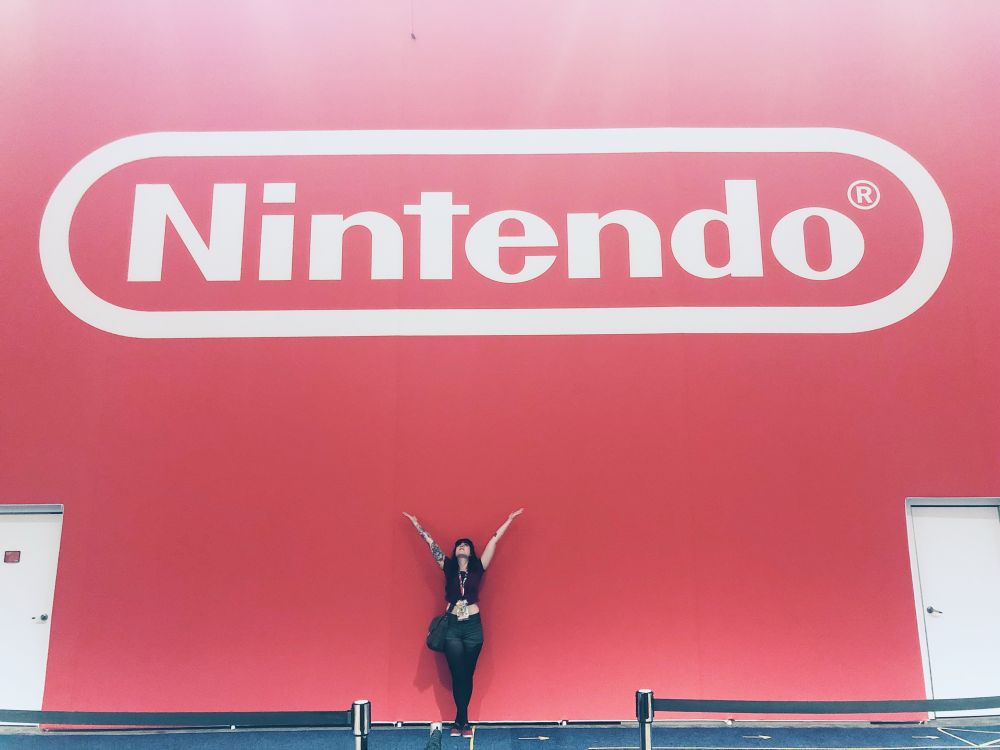 Artist Ky Parker in front of a huge Nintendo logo against a red wall at E3.