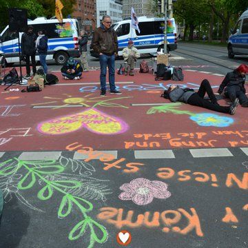 Auf einer mit Kreide bunt bemalten Straße sitzen und liegen Menschen