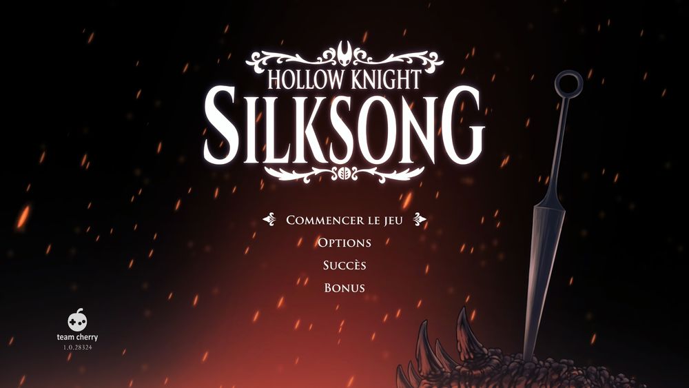 Capture d'écran de l'écran titre d'Hollow Knight: Silksong (Switch 2), c'est le logo du jeu, avec un fond où t'as l'impression que tout a cramé, et l'arme d'Hornet planté dans je sais pas quoi