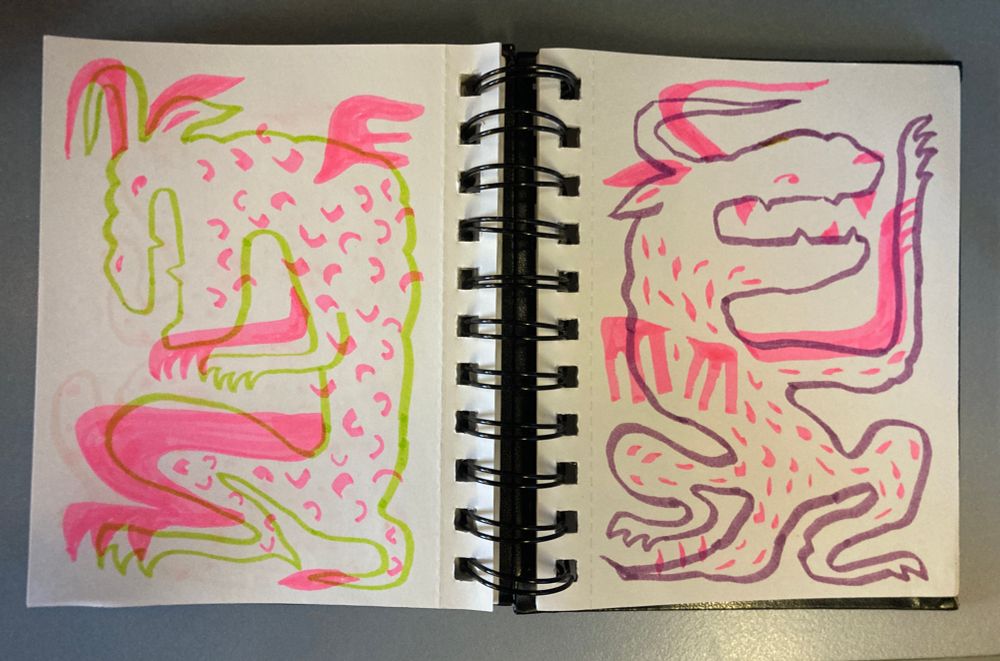 Photo d’un carnet ouvert sur une double page dessinée au feutre et surligneur fluo rose avec des dragons stylisés et rigolos
