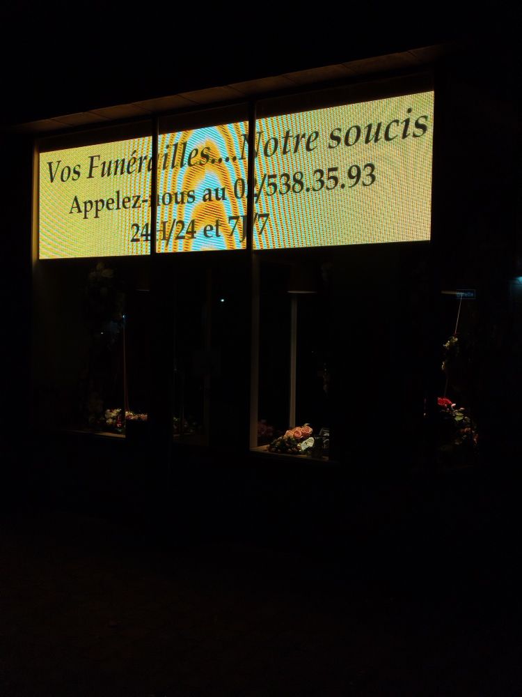Des écrans géants au-dessus d'une vitrine de pompes funèbres : "Vos funérailles....Notre soucis"