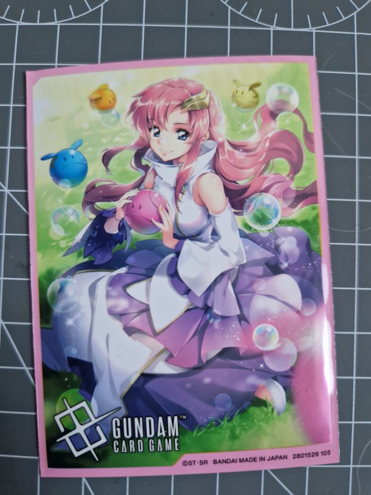 Gundam TCG sleeve with pink border and Lacus with haros and bubbles in a grassy field artwork