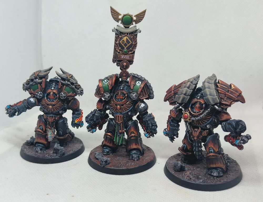 Three kitbashed salamanders Saturnine Command Squad models painted black with flame designs on armour panels and bronze and green accents.