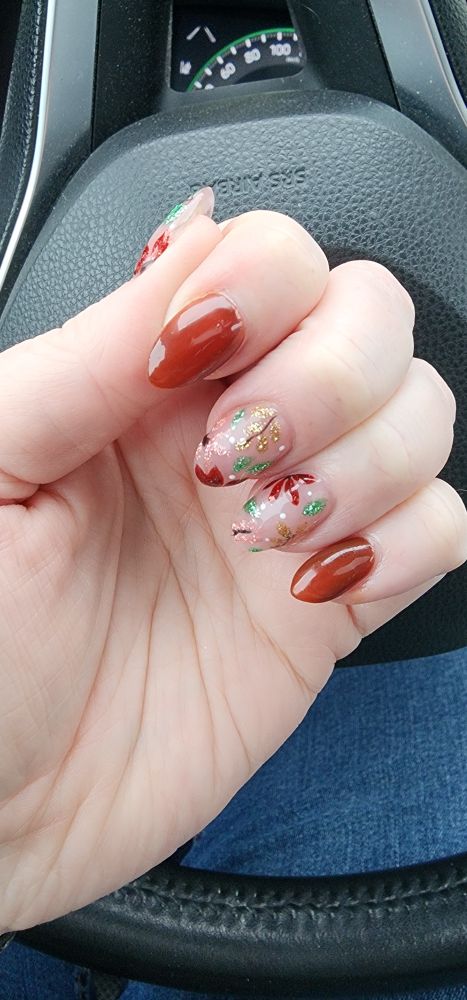 A hand in front of a steering wheel with brown and nude fingernails with a multicoloured leaf design on them 