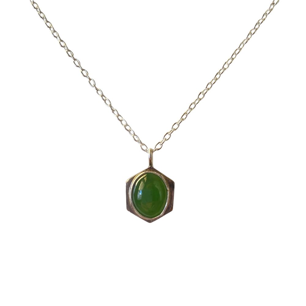 A hexagonal Sterling silver pendant feature a medium green, oval jade cabochon. The pendant is shown on a Sterling silver chain on a white background.