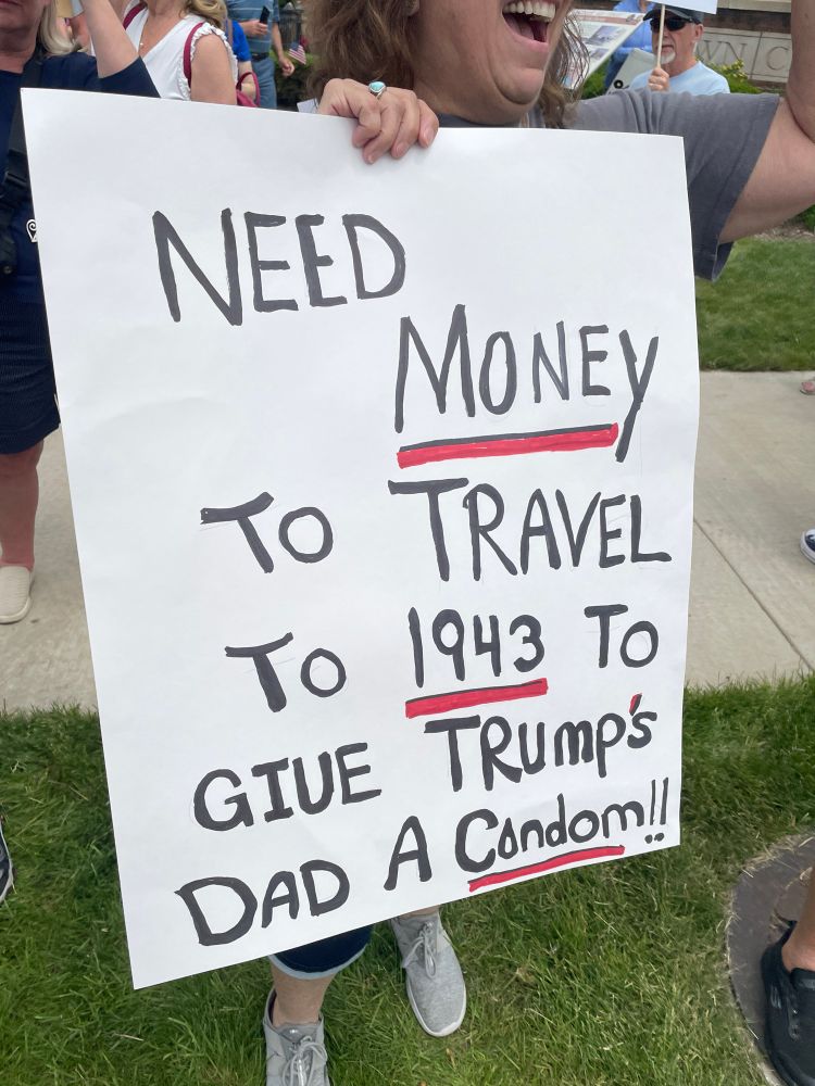 A protest sign reading, “Need money to travel to 1943 to give Trump’s dad a condom!!”