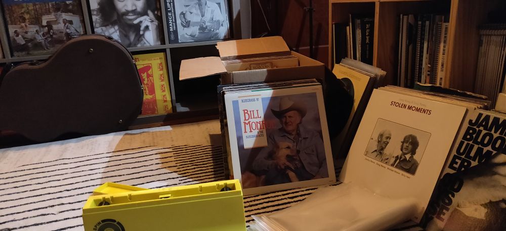 A box of records with a Spin-Clean and some plastic sleeves at hand. Visible records include Bill Monroe, Jimmy and Doug Rainey, and James Blood Ulmer. 