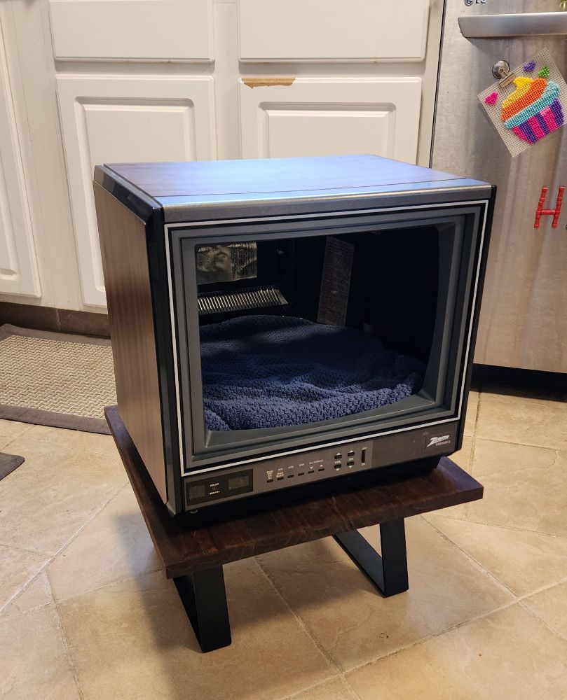 I gutted an old 80s Zenith TV, stained a piece of pine, attached black square legs, and screwed the hollow TV on top of the board. Added a piece of foam cut to fit and wrapped an old towel around the foam for a bed.