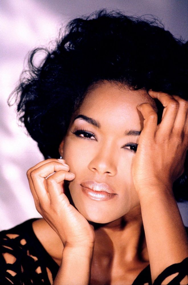 Close up portrait of Angela in front of a lavender background. She is holding her face.