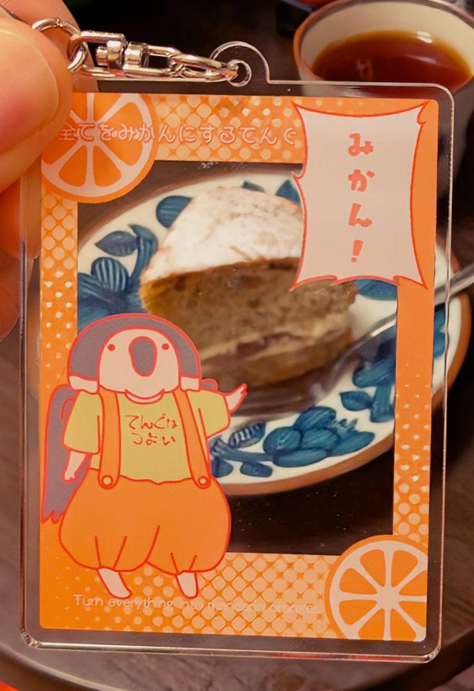 てんぐの子が指を指しながら「みかん！」と言っているアクリルキーホルダー越しに撮ったいちじくのヴィクトリアスポンジ。