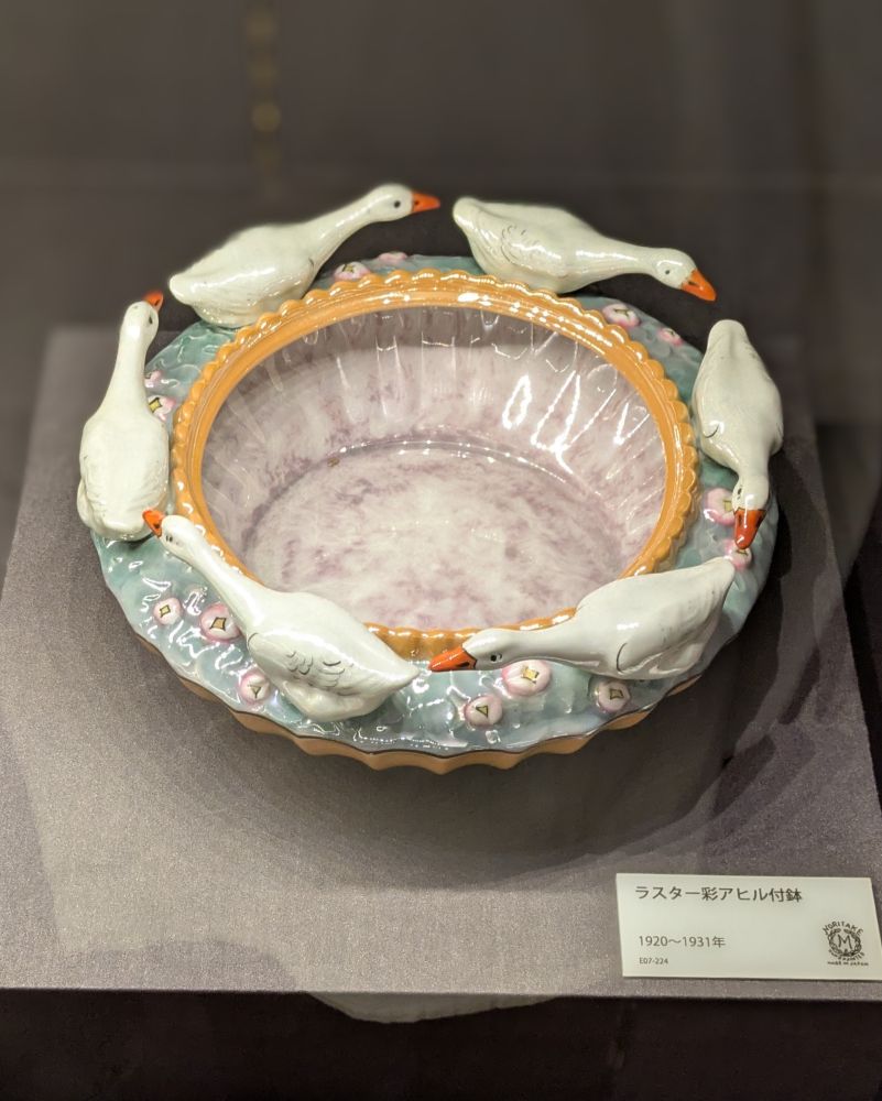 ノリタケミュージアムの撮影可能エリアで撮った「ラスター彩アヒル付鉢」。薄緑色とクリーム色の磁器の鉢のふちを、6羽のアヒルの磁器人形が取り巻いている。