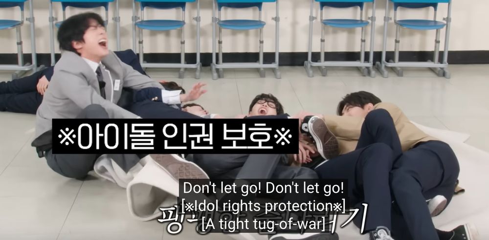 Screenshot from Run Jin where 2 TxT and 2 Enhyphen boys are on the ground playing white radish and Jin is trying to pull them out. Everyone is yelling. There is an *Idol rights protection* block over where Jin is grabbing poor Taehyun... The caption says "Don't let go! Don't let go!"