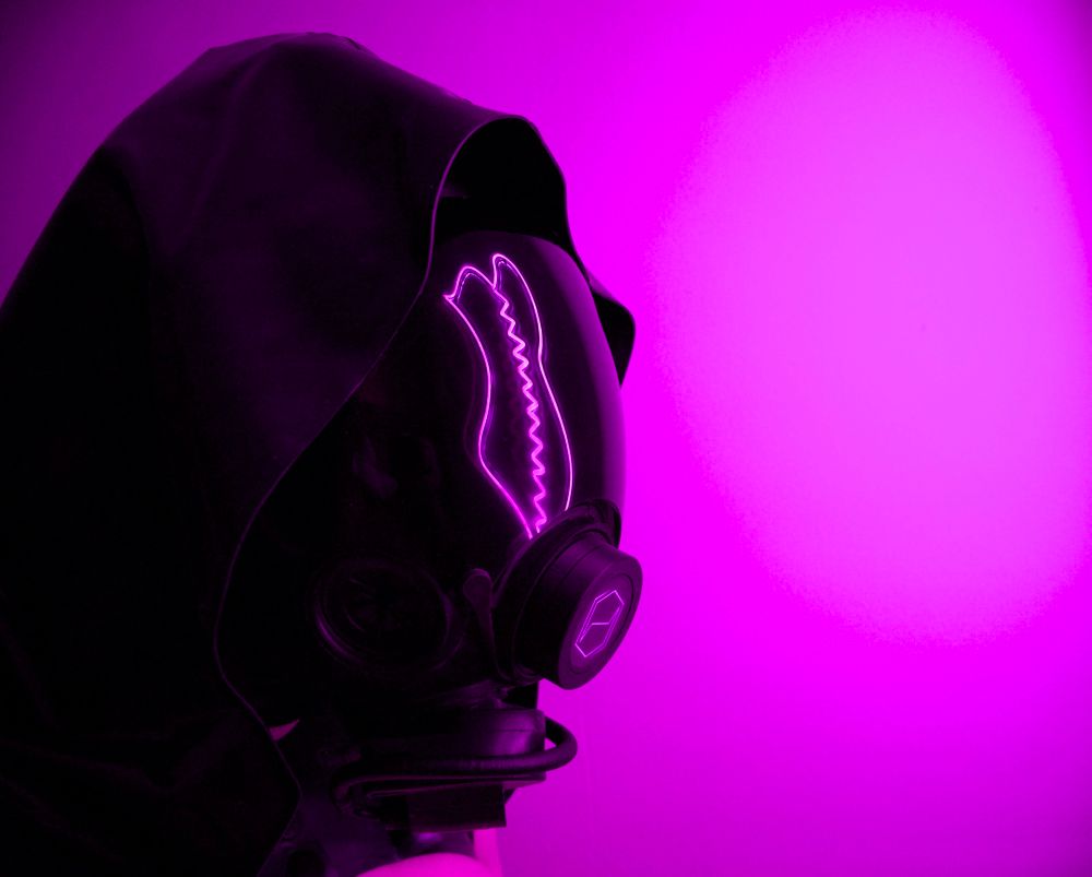 A person with a neon corset reflected in a gas mask visor.  