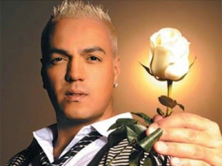 Imagem do Cantor Belo segurando uma rosa branca, a mão com a rosa está em primeiro plano e há um brilho em volta dela no contraplano dourado ao fundo, sugerindo um halo como se a rosa branca fosse luz