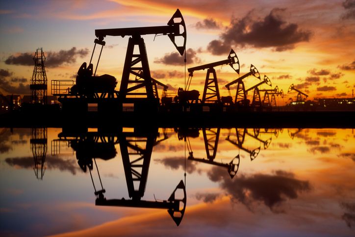 Oil pumps and rigs next to the water at sunset.