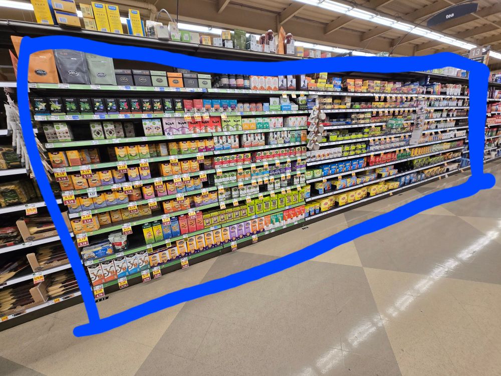 A picture of one side of an aisle of an American grocery store. There is a blue box drawn around the large selection of tea on the shelves. 