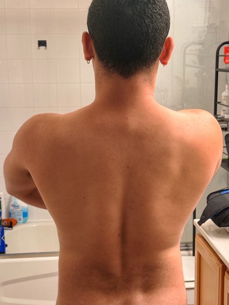 my back as i stand disrobed in my bathroom; i’m about 75% wider at my shoulders than at my waist, and my back shows some subtle musculature in the harsh light