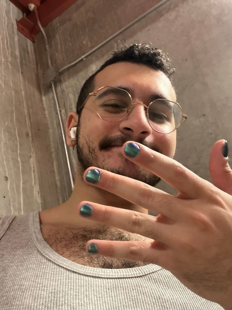 a selfie from within a stairwell; i’m holding my off hand up to the camera to show off my nails; my nails are teal multichrome, with a purple tinge; the polish job is imperfect, slightly bleeding onto my skin