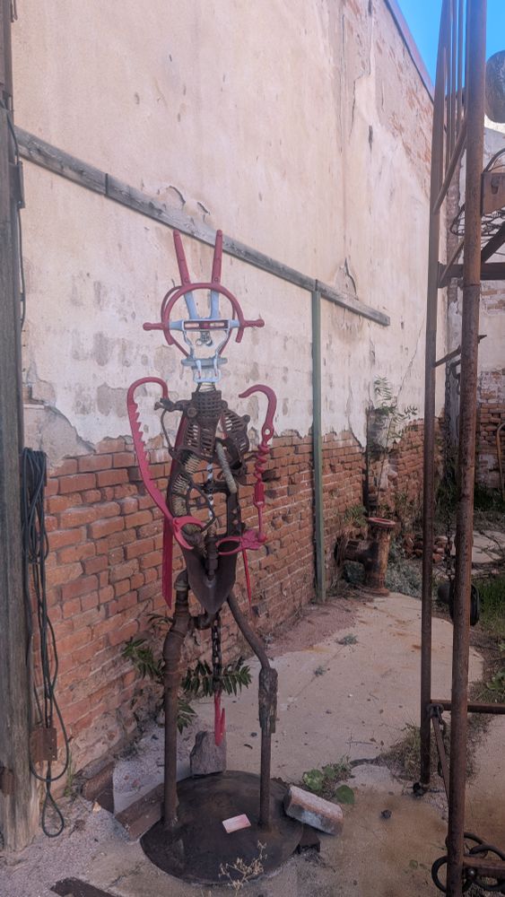 A weird metal figure made of what look like scraps of machinery, with red horns and red arms ending in pincer-like hands 