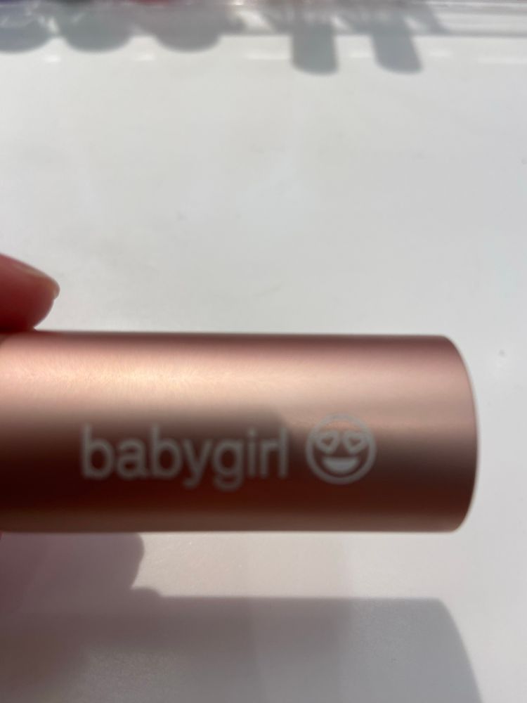 A closed lipstick case with “babygirl” and a heart eye emoji image etched into it.