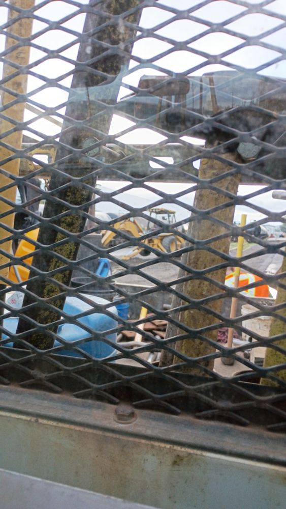 Photo of the back of a work truck window through a headache rack and between tools of the backhoe digging up ties 