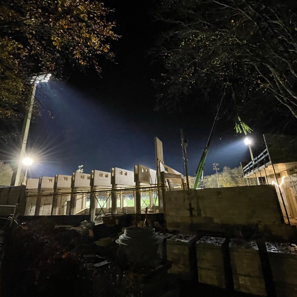 Die Baustelle im Dunkeln von hinten fotografiert, beleuchtet von den Flutlichtern dahinter.