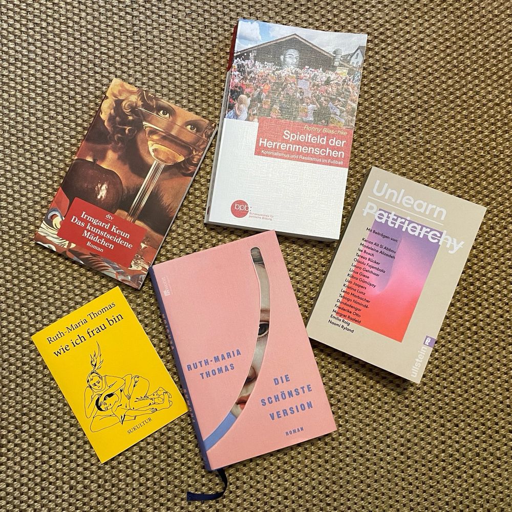 „wie ich frau bin“ und „Die schönste Version“ von Ruth-Maria Thomas; „Das kunstseidene Mädchen“ von Irmgard Keun; „Spielfeld der Herrenmenschen“ von Ronny Blaschke und „Unlearn Patriarchy“ (1) auf Teppichboden.