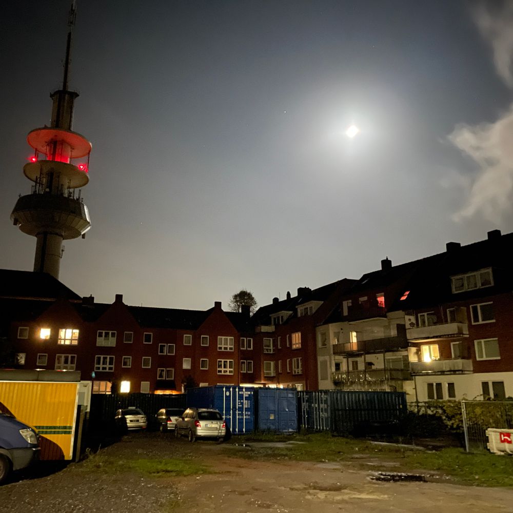 Nachtimpression aus Emden mit Baustellenfahrzeugen, Wohnhäusern, Mond und Wolken.