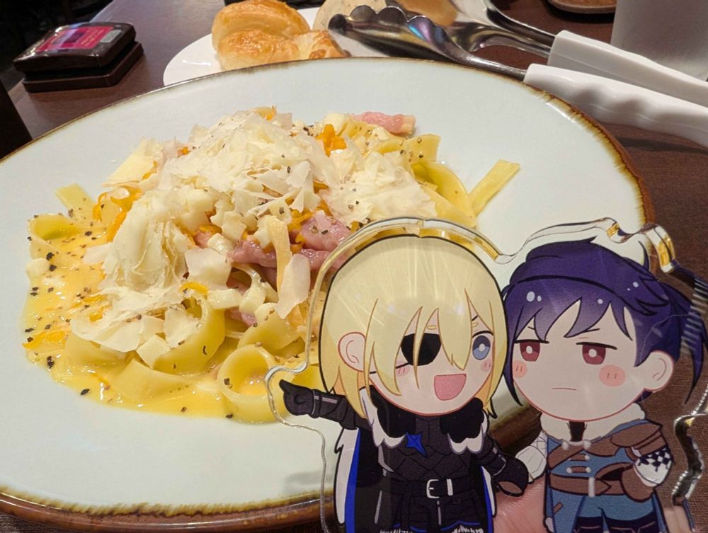 a picture of a dimilix standee in the foreground and pasta + bread in the background. dimitri is pointing towards the food while felix looks on with a blushy frown