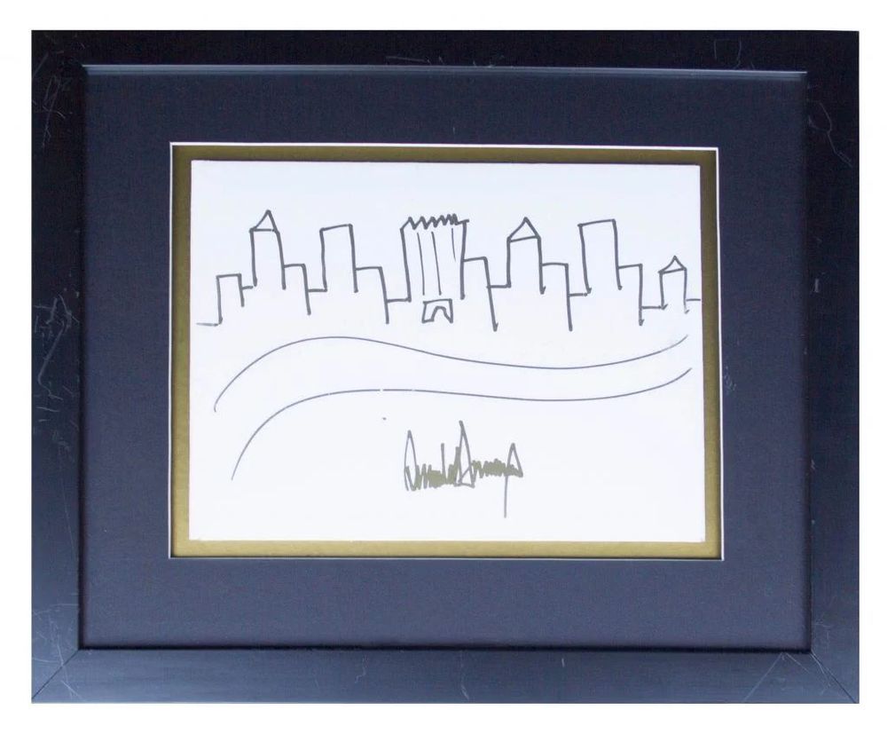 Framed drawing of a simple city skyline, featuring tall rectangular buildings with one in the center marked by jagged lines resembling Trump Tower. Two curved lines below suggest a river or roadway. The drawing is signed “Donald J. Trump” in bold marker at the bottom. The artwork is matted in gold and black and enclosed in a black frame.