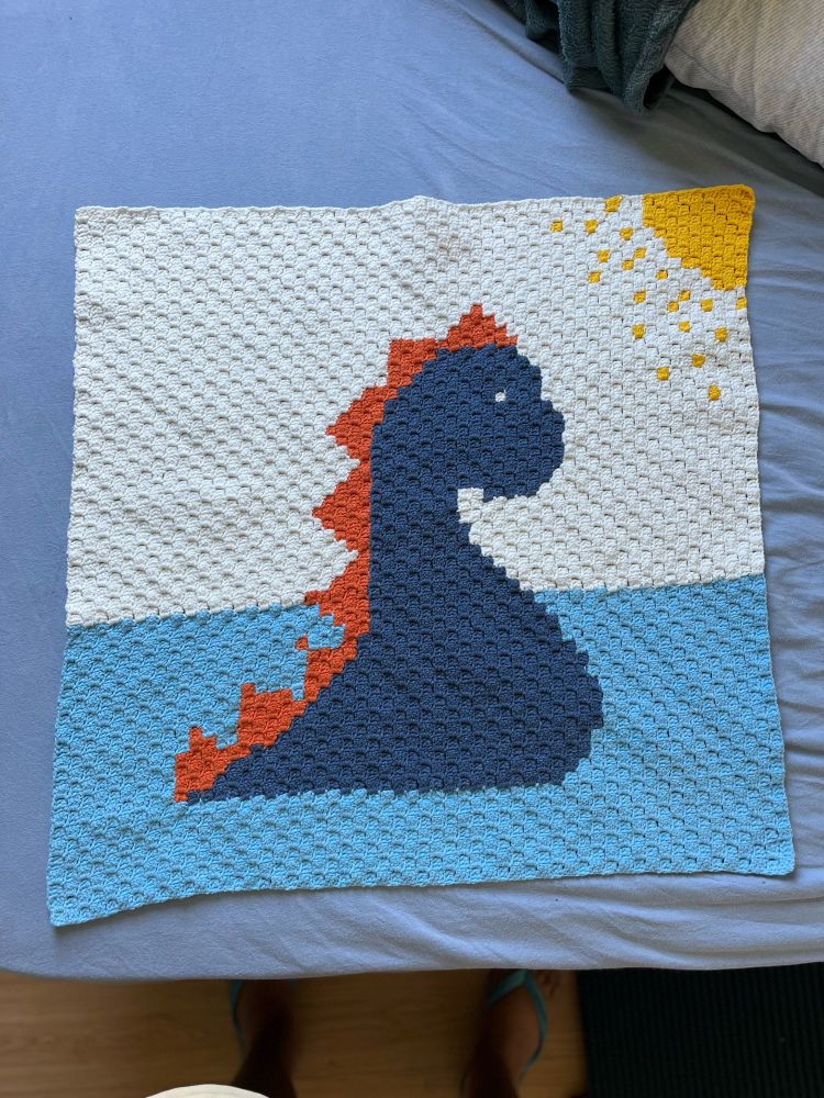 Colcha de crochê com o desenho de um monstro do lago ness. O desenho é formado por quadradinhos