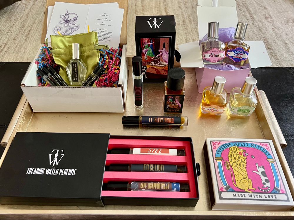 A photo of a tray of perfume bottles from the houses of SYD Botanica, Treading Water, and Hoshi Gato. A decorative box of candle matches is included in the bottom right corner. 