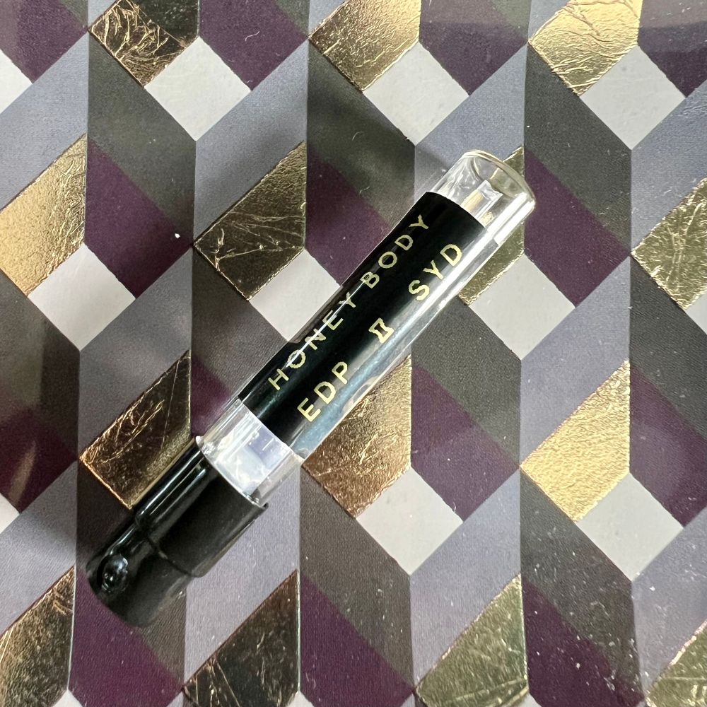 A photo of an empty sample vial of the perfume Honey Body by SYD Botanica. 